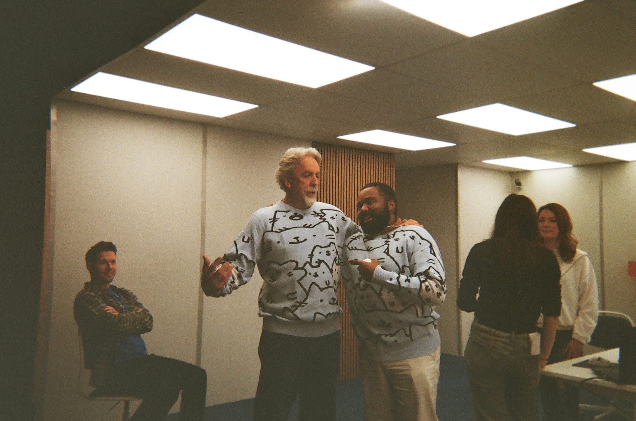 Crew and cast sharing a laugh in matching cat-print sweaters between setups